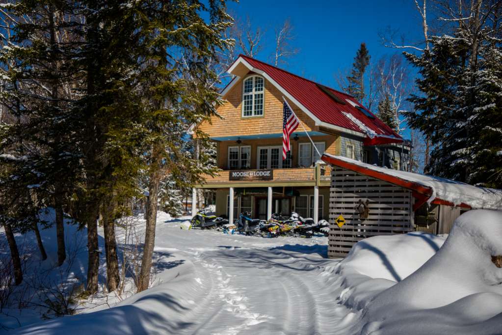 Snow-covered cabin with red roof in a sunny winter forest.