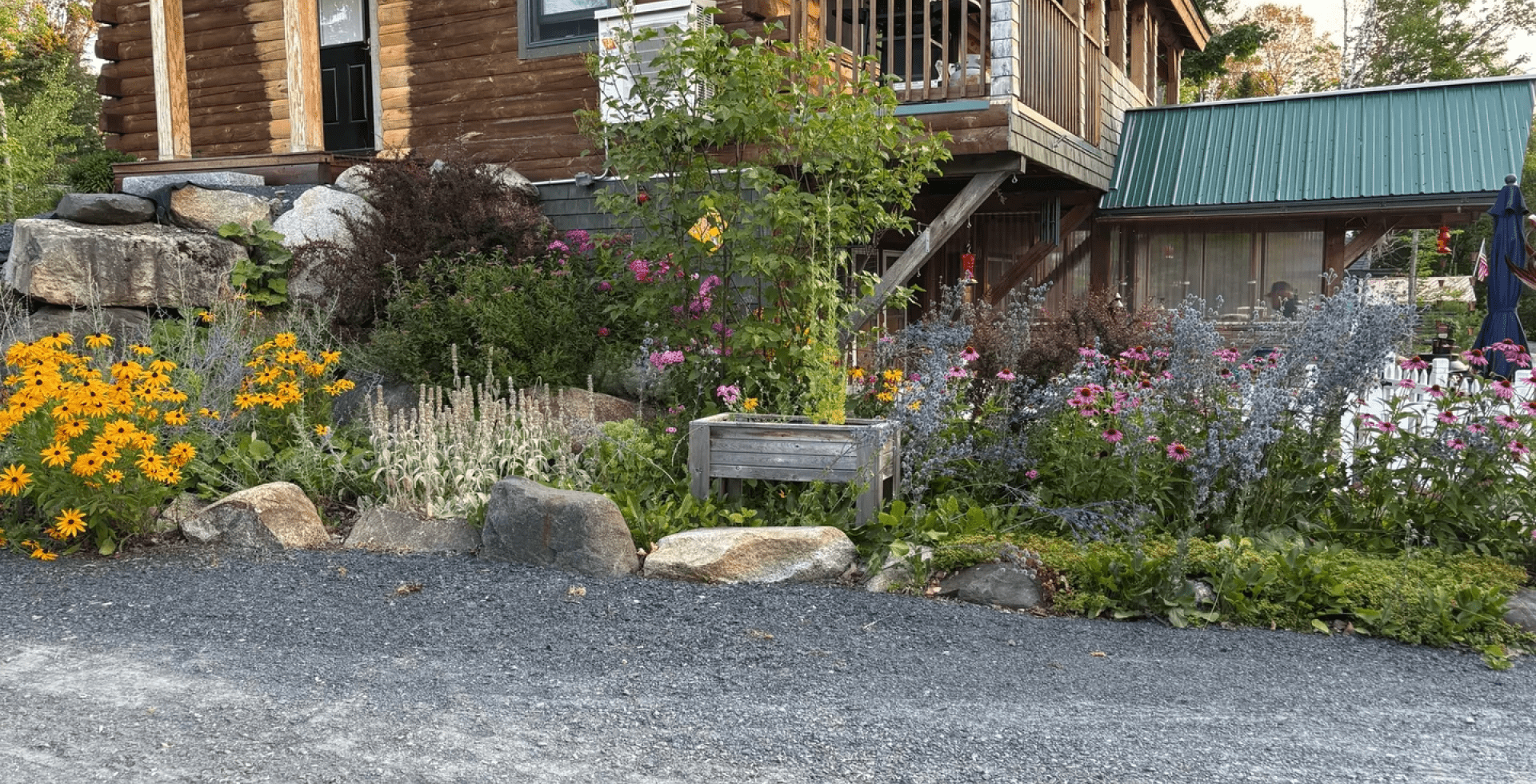 A rustic wooden sign in a colorful garden outside a wooden building.