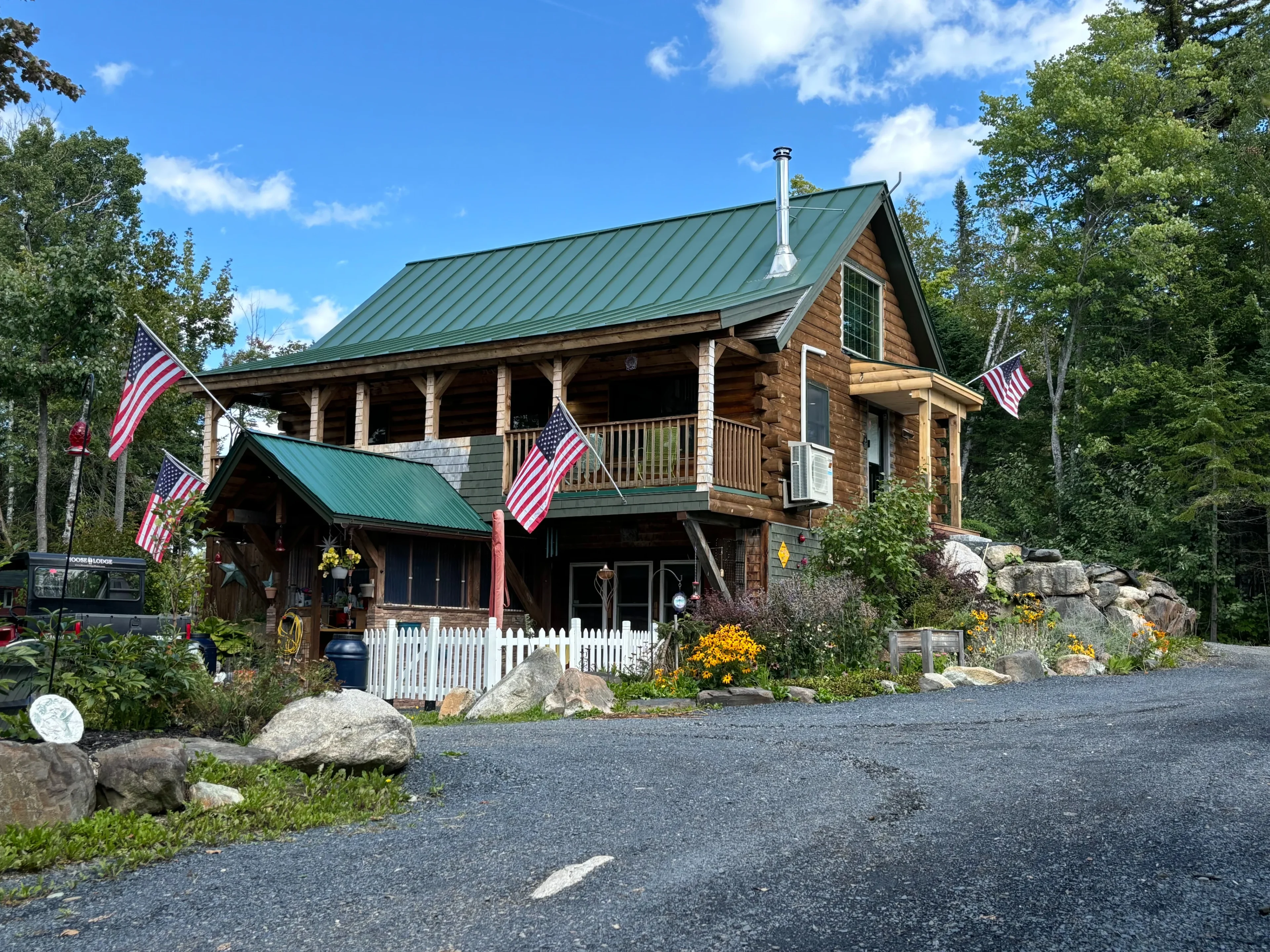 A rustic house with American flags and a green roof on a sunny day.